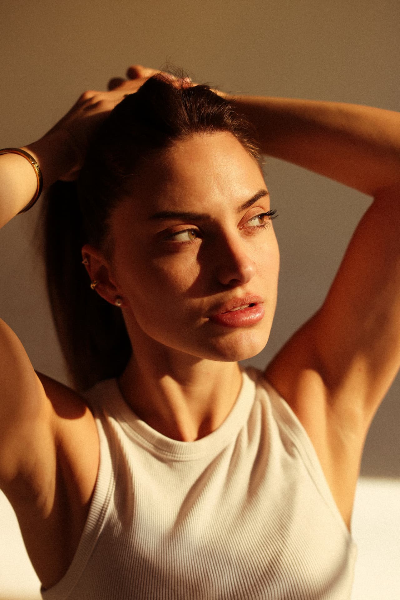 Close-up portrait in a white ribbed tank with hands lifting dark hair