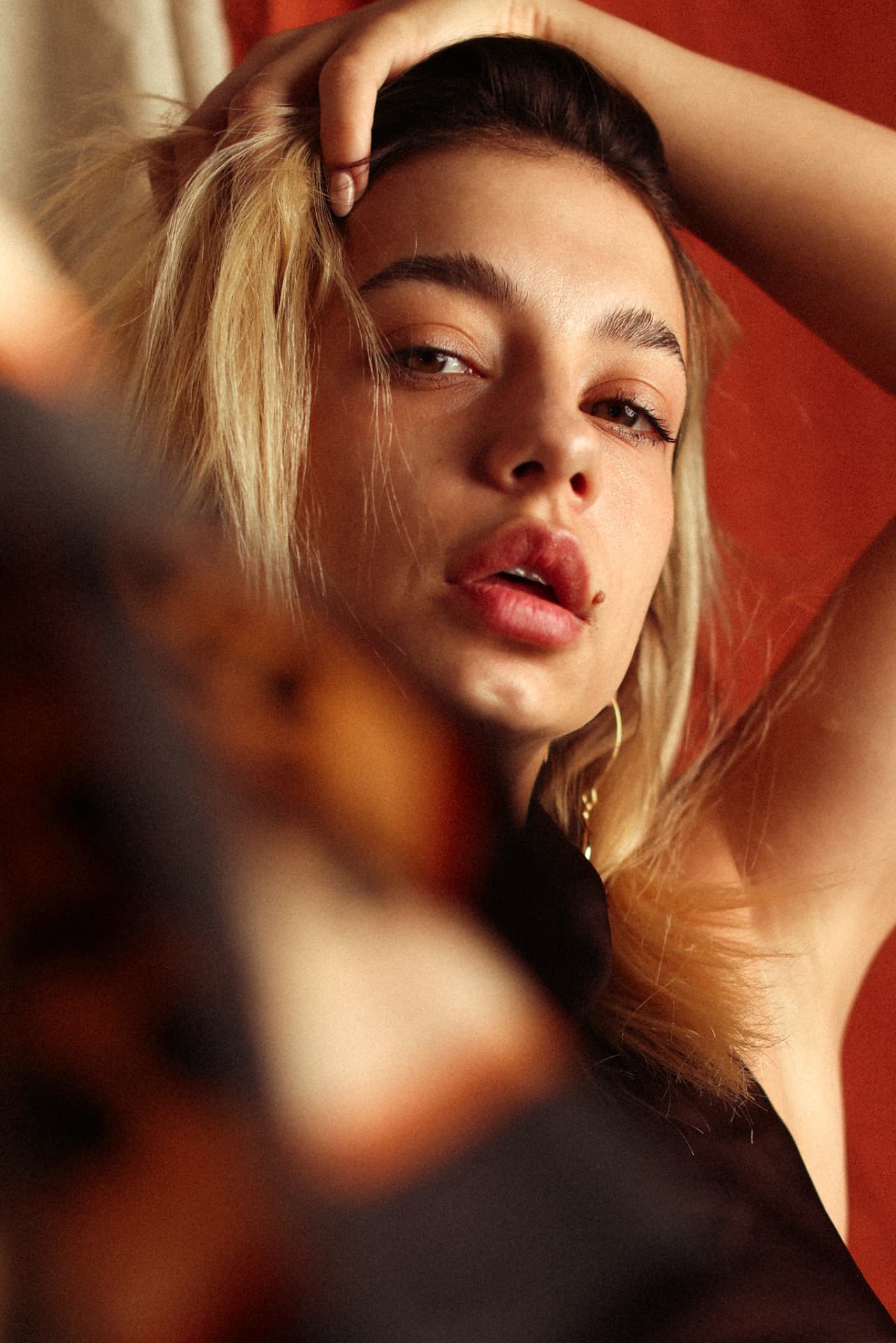 Blonde model with arm raised against red backdrop