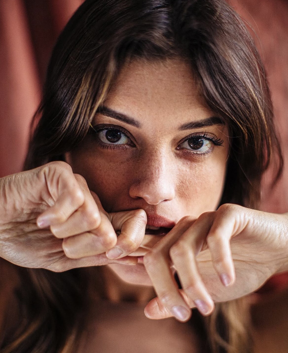 Close-up portrait with hands against a warm pink backdrop