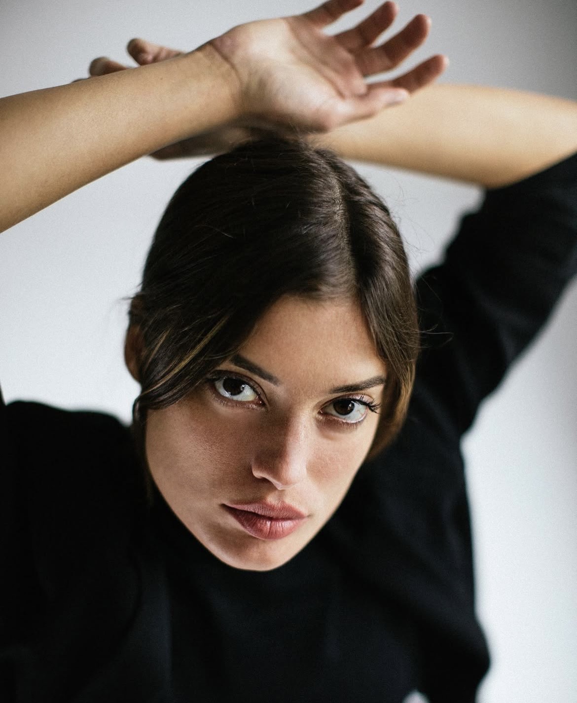 Brunette with arms raised against a white backdrop