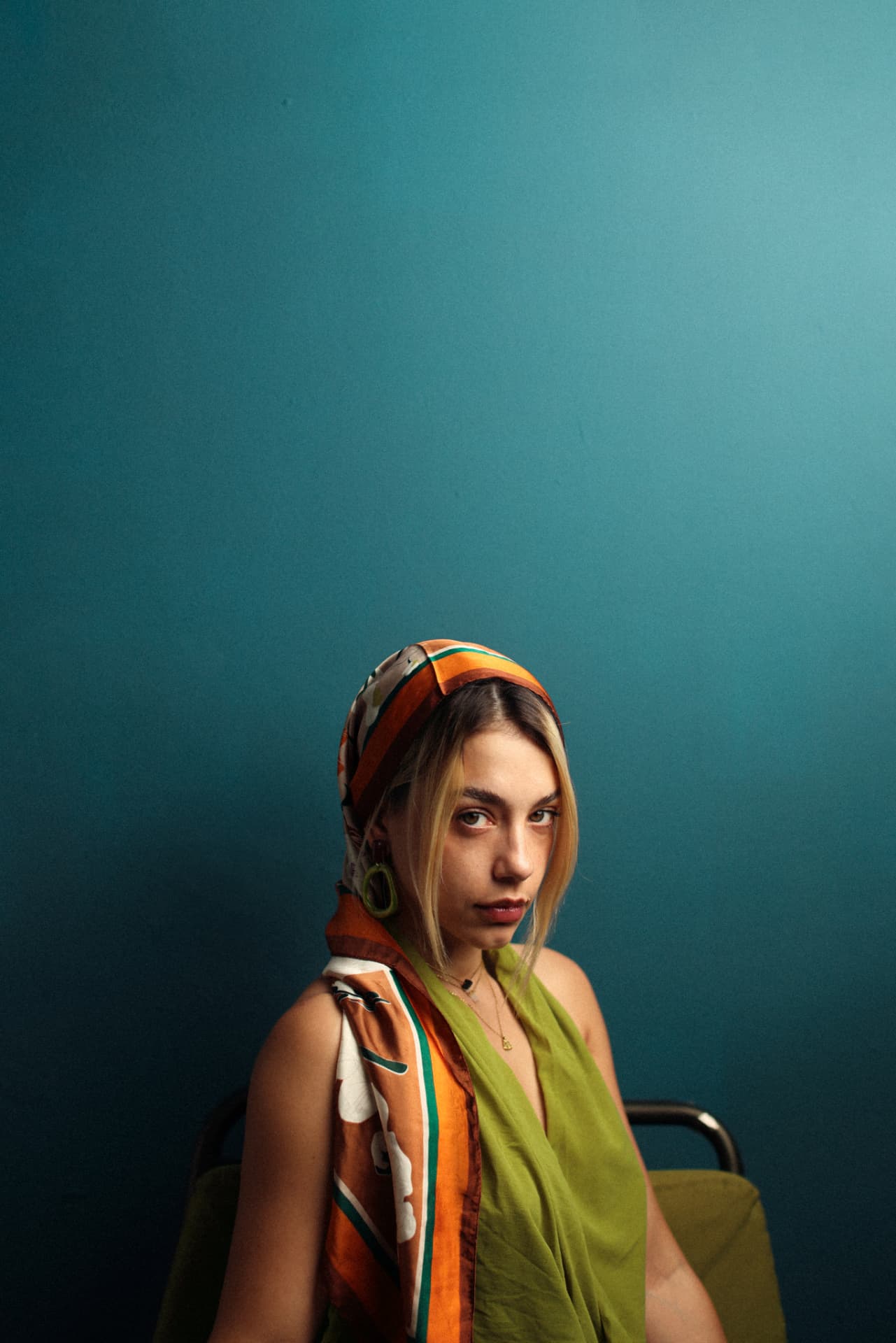 Seated portrait with headscarf against teal wall