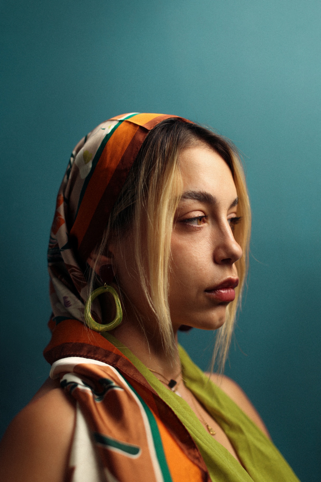 Profile portrait with patterned headscarf against teal wall